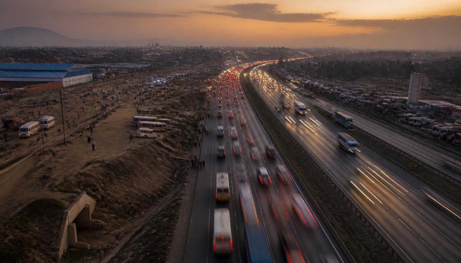 A Kenyan highway at dusk with traffic and roadside activity